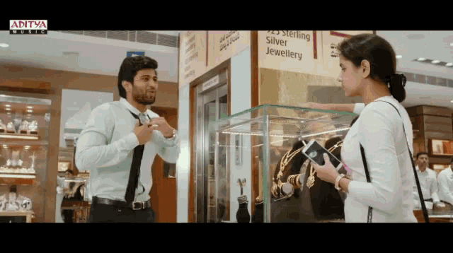 a man in a tie is talking to a woman in front of a sign for sterling silver jewellery