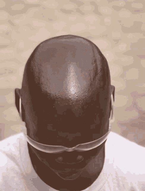 a bald man wearing sunglasses and earbuds looks down