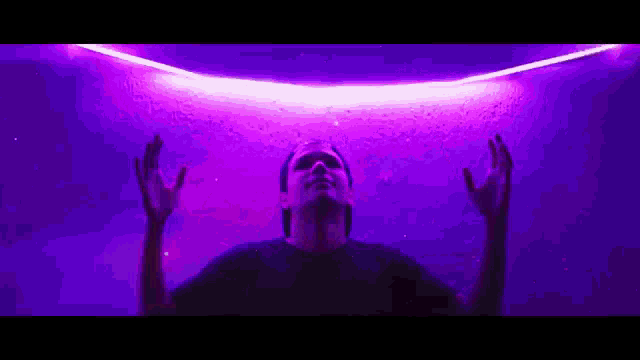 a man is standing in front of a purple light with his arms outstretched .