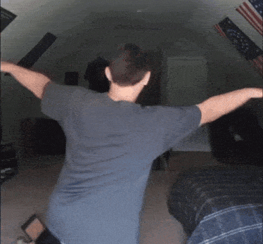 a man in a grey shirt is dancing in a bedroom with american flags on the ceiling