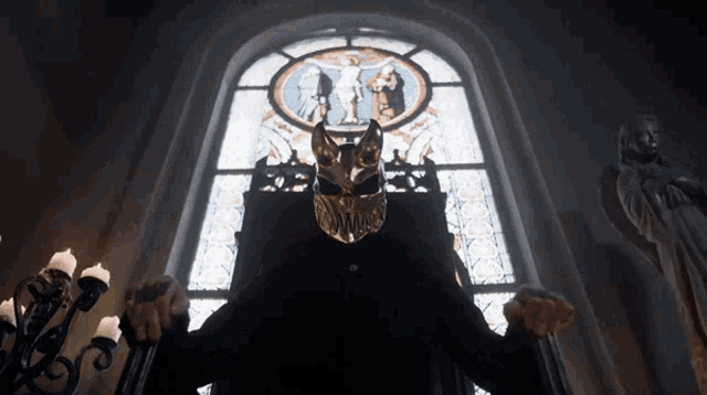 a man wearing a mask sits on a throne in front of a stained glass window