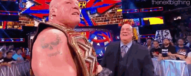 a man in a suit and tie is standing next to a wrestler in a wrestling match .