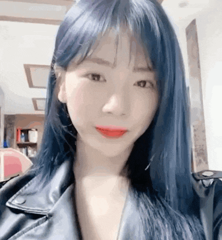 a young woman with blue hair and red lipstick is wearing a leather jacket .