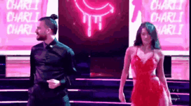a man and a woman are dancing on a stage in front of a neon sign that says charli