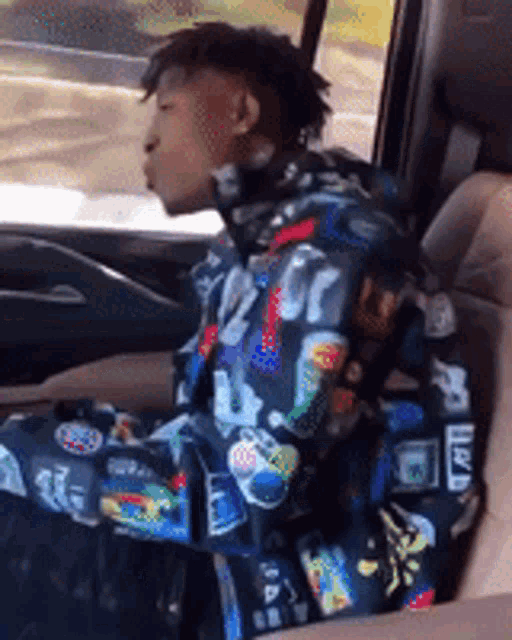 a man in a colorful jacket is sitting in the driver 's seat of a car .