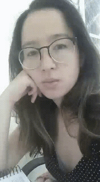 a woman wearing glasses looks at the camera with her hand on her chin