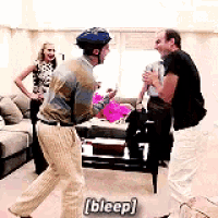 a man wearing a helmet is dancing in a living room while a woman looks on .