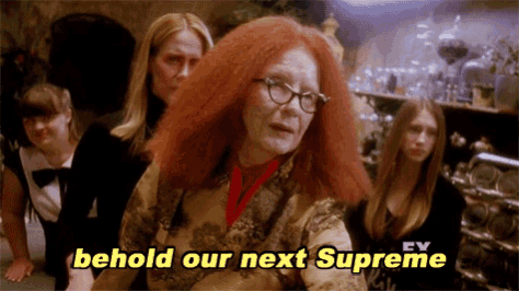 a woman with red hair and glasses is standing in front of a group of women .