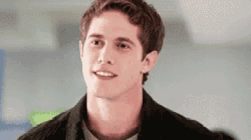 a young man in a black jacket is smiling while standing in a room .