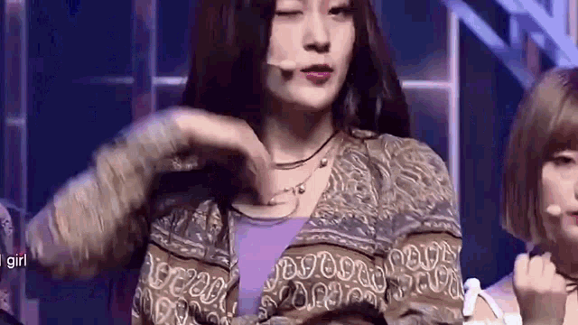 a woman is making a heart shape with her hands while singing into a microphone .