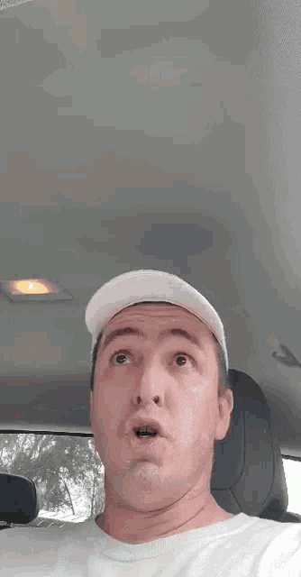 a man wearing a white hat is making a funny face while sitting in the back seat of a car .