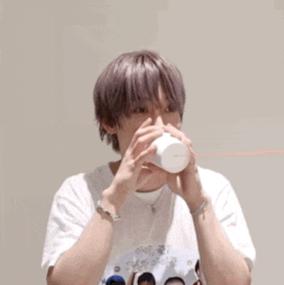 a young man with purple hair is drinking from a paper cup .