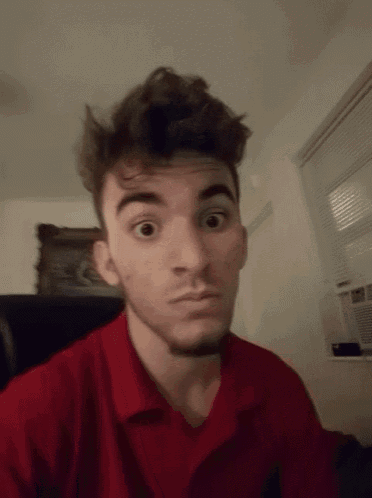 a young man in a red shirt makes a surprised face