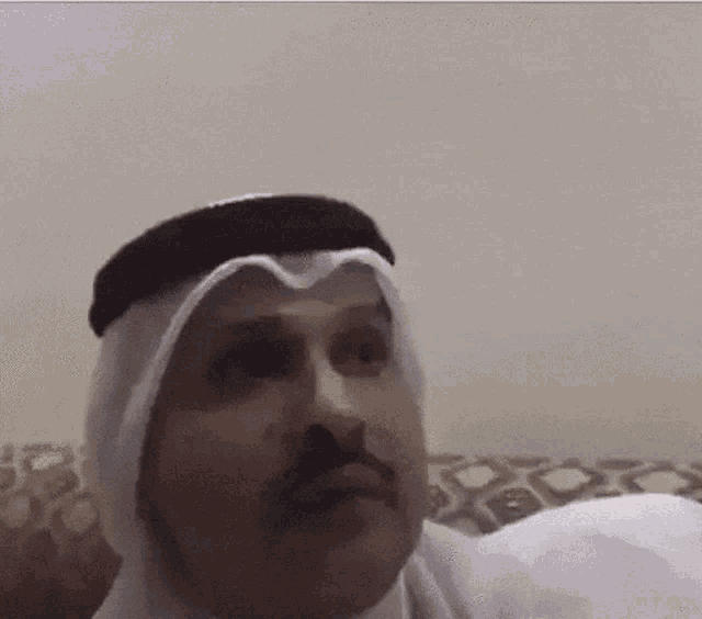 a man in a turban is sitting on a couch and looking at the camera .