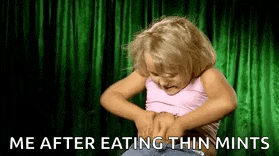 a little girl is eating thin mints and looking at her stomach .
