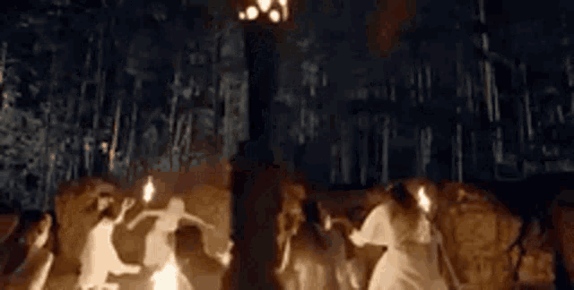 a group of people are dancing around a fire in a forest at night .
