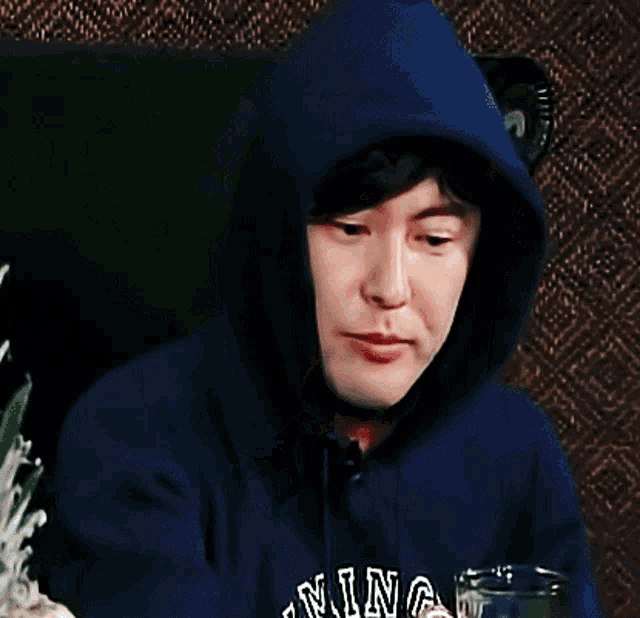 a person wearing a hoodie that says ' ming ' on it drinking from a glass