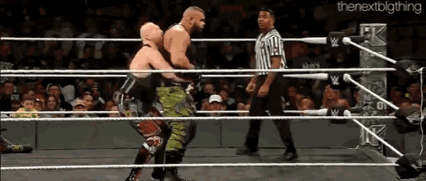 two wrestlers are fighting in a ring with a referee standing between them and a sign that says the nextbigthing