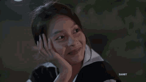 a young girl is smiling with her hand on her face and looking up .