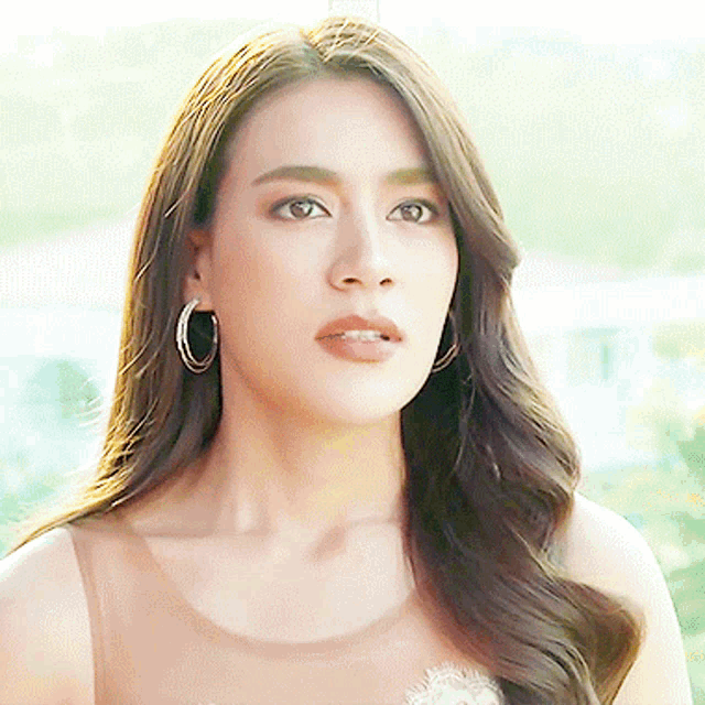 a woman wearing hoop earrings looks at the camera with a serious look on her face