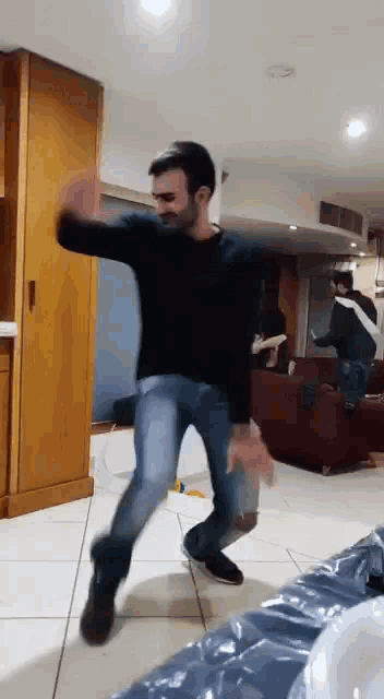 a man in a black shirt and jeans is dancing in a room .