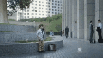 a young boy is standing on a sidewalk talking on a cell phone .