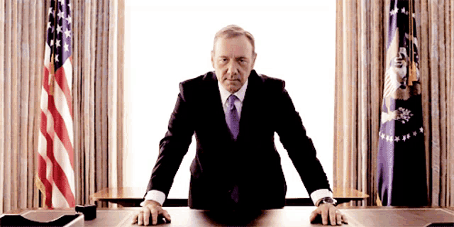 a man in a suit and tie stands in front of a desk