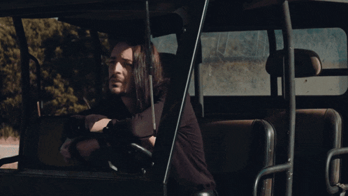 a man with long hair is driving a vehicle with a sticker that says ' jeep ' on it