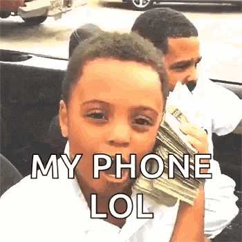 a young boy is holding a stack of money in his hand and talking on a cell phone .