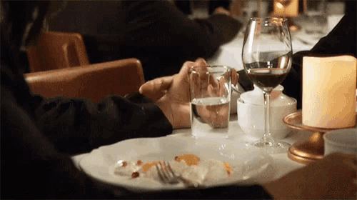 a person holding a glass of water next to a wine glass and a candle