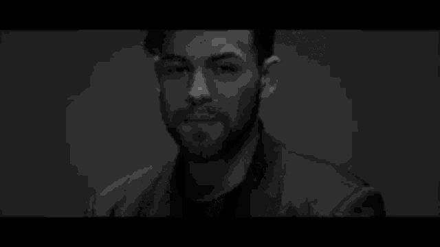 a black and white photo of a man with a beard in a dark room .