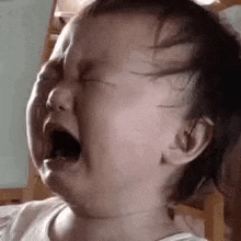 a close up of a baby crying with his mouth open .
