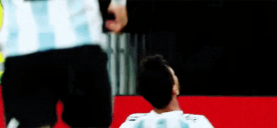 a soccer player is laying on the ground with his head on the ground while another player stands behind him .