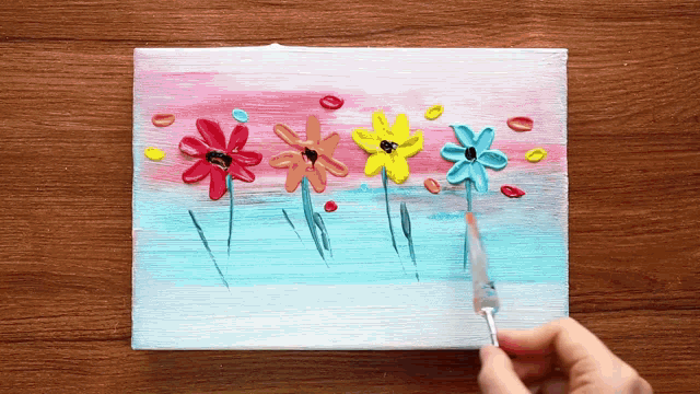 a person is painting flowers with a brush on a canvas