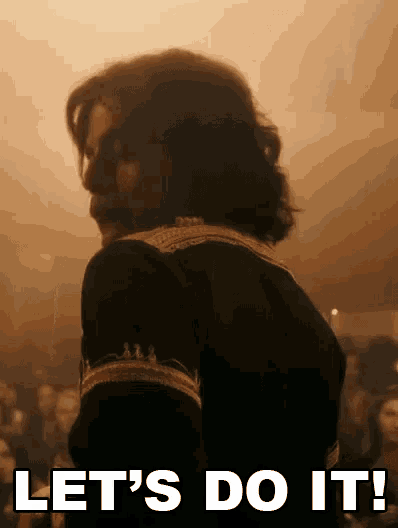 a man with long hair and a beard is standing in front of a crowd and saying `` let 's do it '' .
