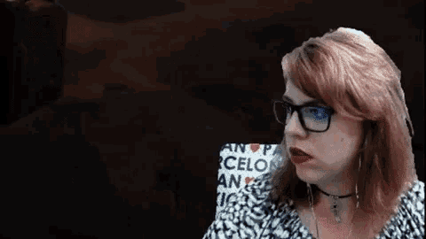 a woman wearing glasses and a choker is looking at something in the dark .