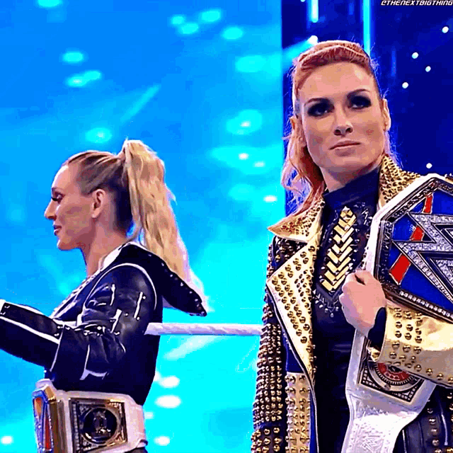 a couple of women standing next to each other on a stage holding championship belts .