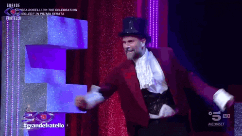 a man in a top hat is dancing on a stage with the words grande fratello on the bottom right