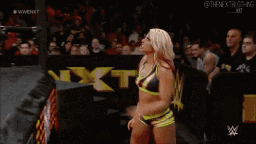a woman is standing in a wrestling ring in front of a crowd while wearing a green and black top .