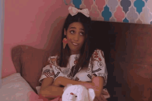 a girl with an ice cream cone on her face is sitting on a bed holding a teddy bear