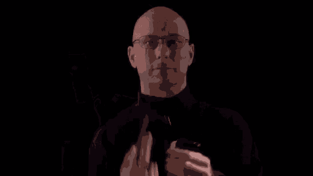 a bald man with glasses is holding a black iphone in his hand .