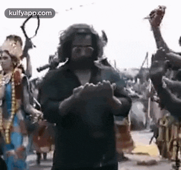 a man with a beard is standing in front of a crowd of people holding his hands together .