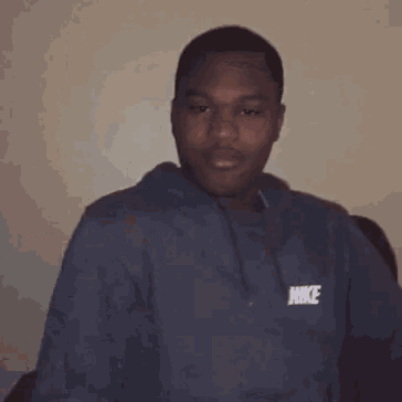 a young man wearing a blue nike hoodie looks at the camera
