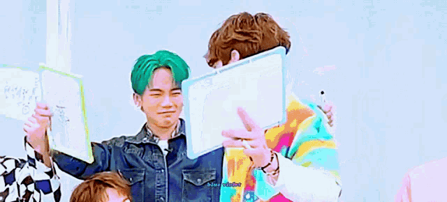 a group of young men with green hair are standing next to each other and one of them is holding a white board .