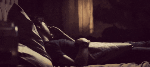 a man is laying on a bed in a dark room with a window in the background