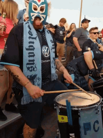 a man wearing a mask and a scarf that says always plays drums