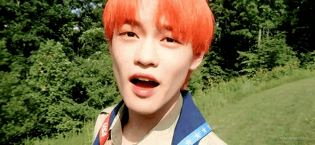 a close up of a person with red hair standing in a field with trees in the background .