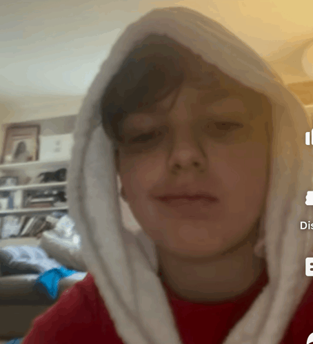 a boy wearing a red shirt and a white hooded sweatshirt looks at the camera