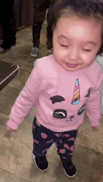 a little girl wearing a pink unicorn shirt and blue pants