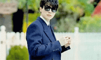 a man in a suit and sunglasses is standing in front of a fence .